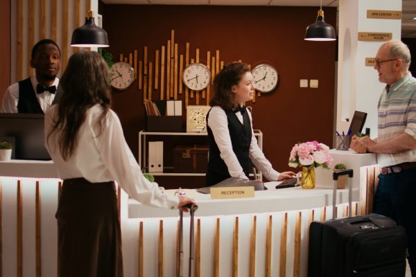 Elderly people arriving in hotel lobby to see accommodation, travelling on retirement holiday with all inclusive room services. Husband and wife talking to concierge about senior travel offers.