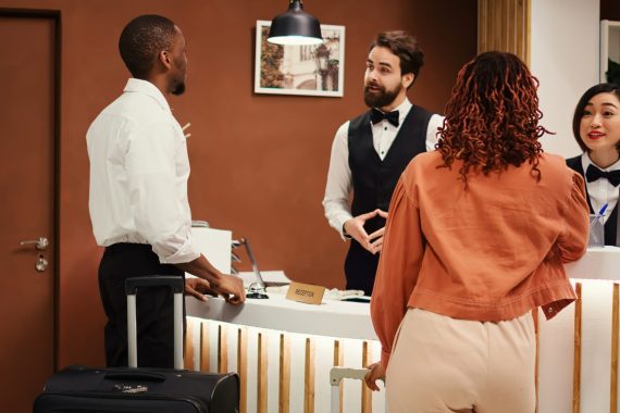 Hotel manager handing arriving visitors booking reservation file to receptionists during check in. Business travelling guests being assisted by helpful concierge staff coworkers inside reception lobby