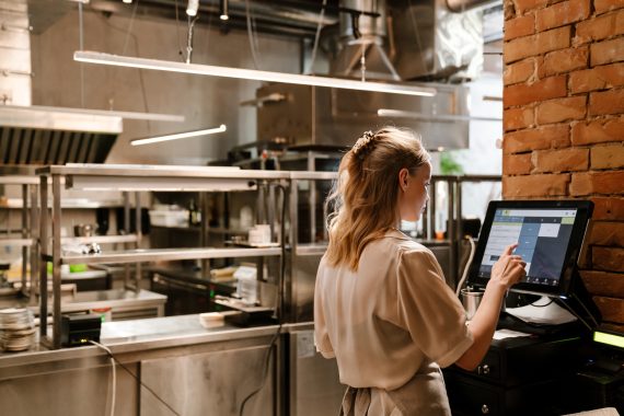 Young white woman waitress wearing apron using computer terminal while working in restaurant