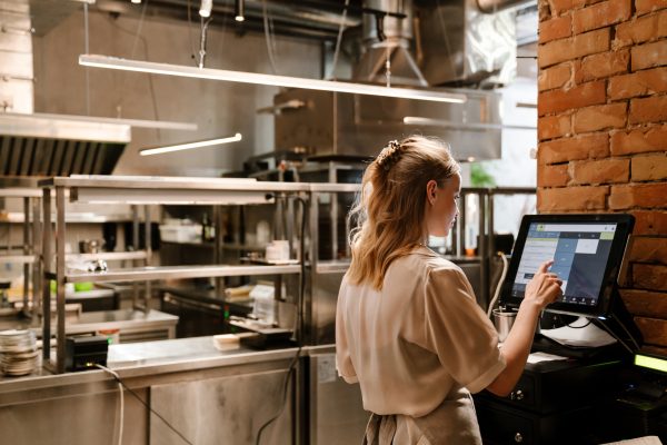 Young white woman waitress wearing apron using computer terminal while working in restaurant