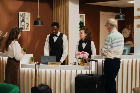 Old people ring service bell at hotel, receptionist ensuring easy check in process and helping tourists with room reservation. Couple on retirement trip arriving at all inclusive resort. Tripod shot.